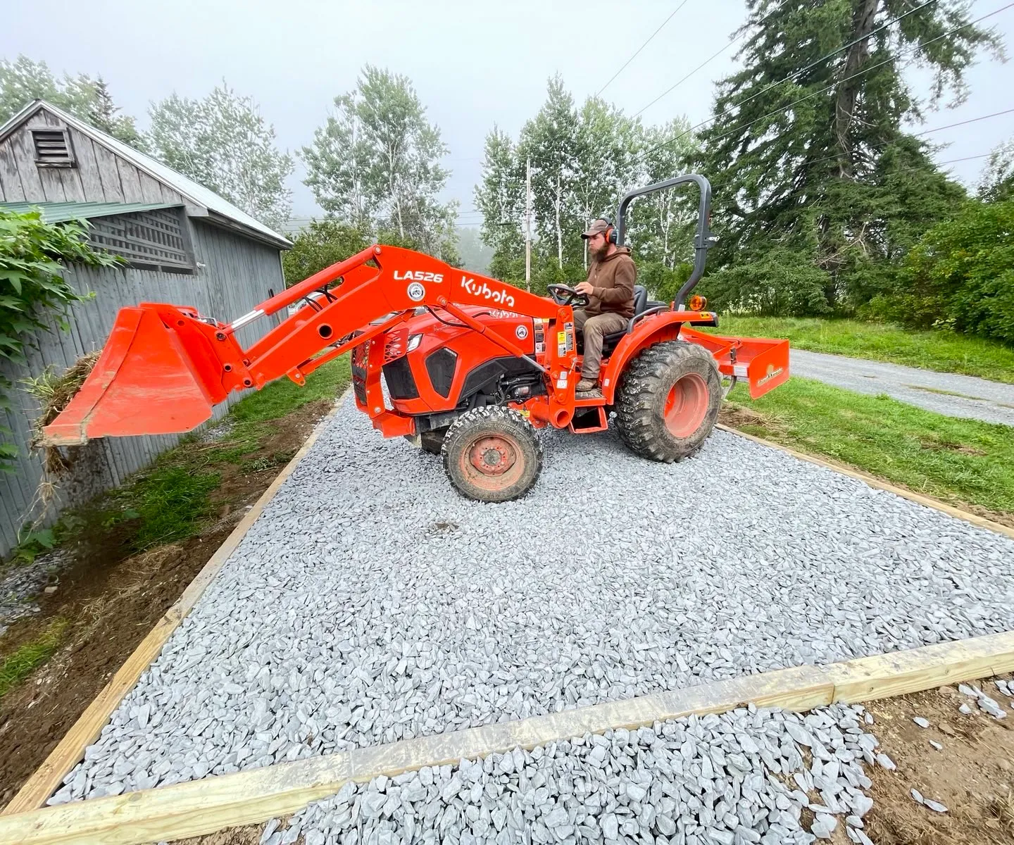 Orange tractor on a crushed-stone pad with timber edging, beside a building.